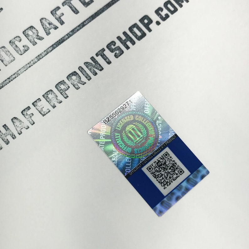 May include: A holographic sticker with a blue border and a QR code. The sticker has the text "Officially Licensed Collegiate Product" and "Licensed Collegiate Products" with a logo of a building with columns and the text "Officially Licensed Collegiate Products" in a circle.