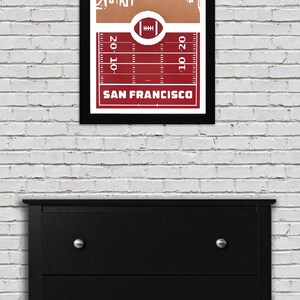 May include: A framed print of a red and white football field with a white outline of the San Francisco skyline. The text "SAN FRANCISCO" is printed below the field.