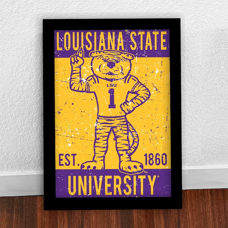 May include: Framed print with the Louisiana State University tiger mascot in a number 1 jersey. The print has a distressed, vintage style, with the text "LOUISIANA STATE UNIVERSITY" and "EST. 1860". The colours are purple and gold.