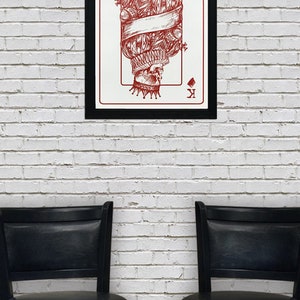 May include: A framed print of a red and white playing card featuring the King of Diamonds. The card depicts a skull wearing a crown and a ruff collar.