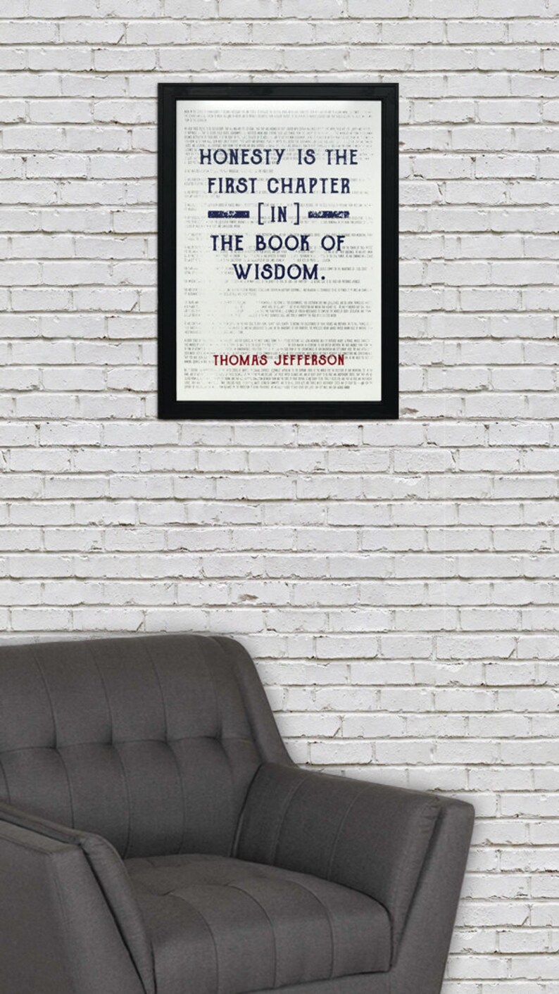 May include: A framed print with the quote "HONESTY IS THE FIRST CHAPTER [IN] THE BOOK OF WISDOM" by Thomas Jefferson. The text is in black and blue on a white background, framed in black. A gray armchair is in the foreground.