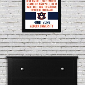 K&ouml;nnte beinhalten: Ein gerahmter Druck mit den Texten des Kampfliedes der Auburn University. Die Texte sind in schwarzer Schrift auf wei&szlig;em Hintergrund mit einem blauen und orangen Streifen unten. Das Logo der Auburn University befindet sich in der Mitte des blauen und orangen Streifens. Der Text lautet: "WAR EAGLE, FLY DOWN THE FIELD, EVER TO CONQUER, NEVER TO YIELD: WAR EAGLE. FEARLESS AND TRUE. FIGHT ON YOU ORANGE AND BLUE. GO! GO! GO! ON TO VICT'RY, STRIKE UP THE BAND. GIVE 'EM HELL, GIVE 'EM HELL, STAND UP AND YELL, HEY! WAR EAGLE, WIN FOR AUBURN, POWER OF DIXIELAND! FIGHT SONG AUBURN UNIVERSITY"