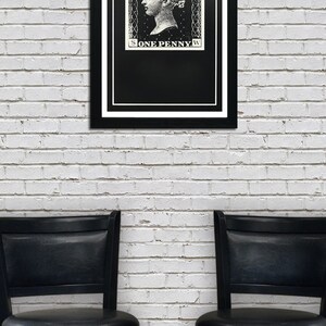 May include: A black framed print of a vintage postage stamp featuring a woman's profile with the text "POSTAGE ONE PENNY" on a white brick wall background. Two black bar stools are in the foreground.
