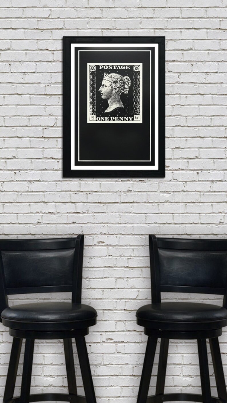 May include: A black framed print of a vintage postage stamp featuring a woman's profile with the text "POSTAGE ONE PENNY" on a white brick wall background. Two black bar stools are in the foreground.