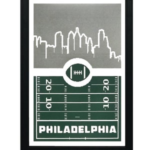 May include: A framed print with a silver cityscape silhouette of Philadelphia, a green football field with yard lines, and the word "PHILADELPHIA" in white text.
