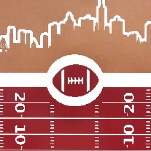 May include: A red and white football field with a white circle containing a football in the center. The top of the image shows a white silhouette of a city skyline against a brown background.