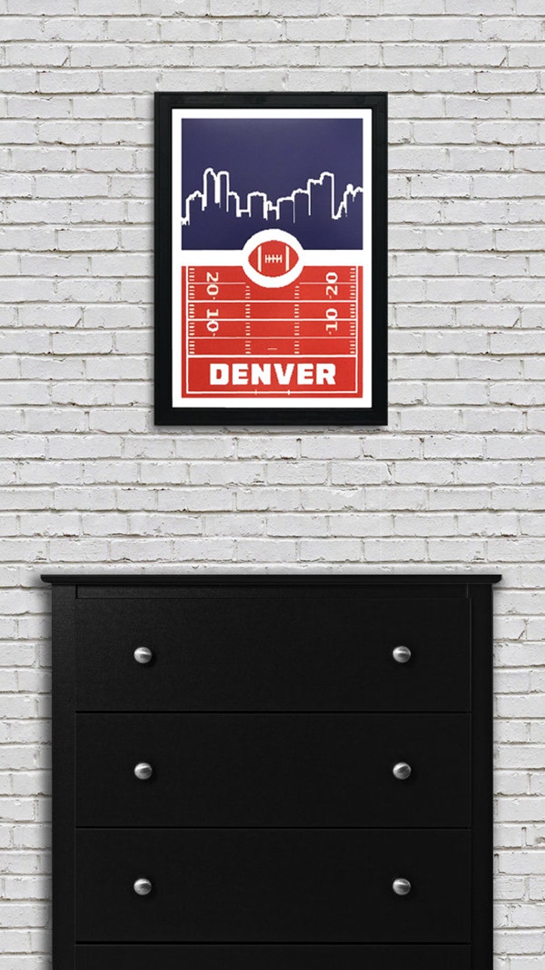 May include: A framed print of a red and blue football field with a white silhouette of the Denver skyline. The text "DENVER" is printed in white at the bottom of the field.