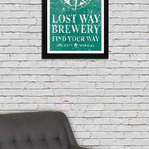 May include: A framed green and white sign with a compass and the text "Lost Way Brewery Find Your Way - Holdrege, Nebraska".