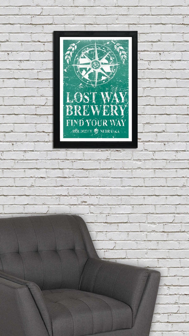 May include: A framed green and white sign with a compass and the text "Lost Way Brewery Find Your Way - Holdrege, Nebraska".