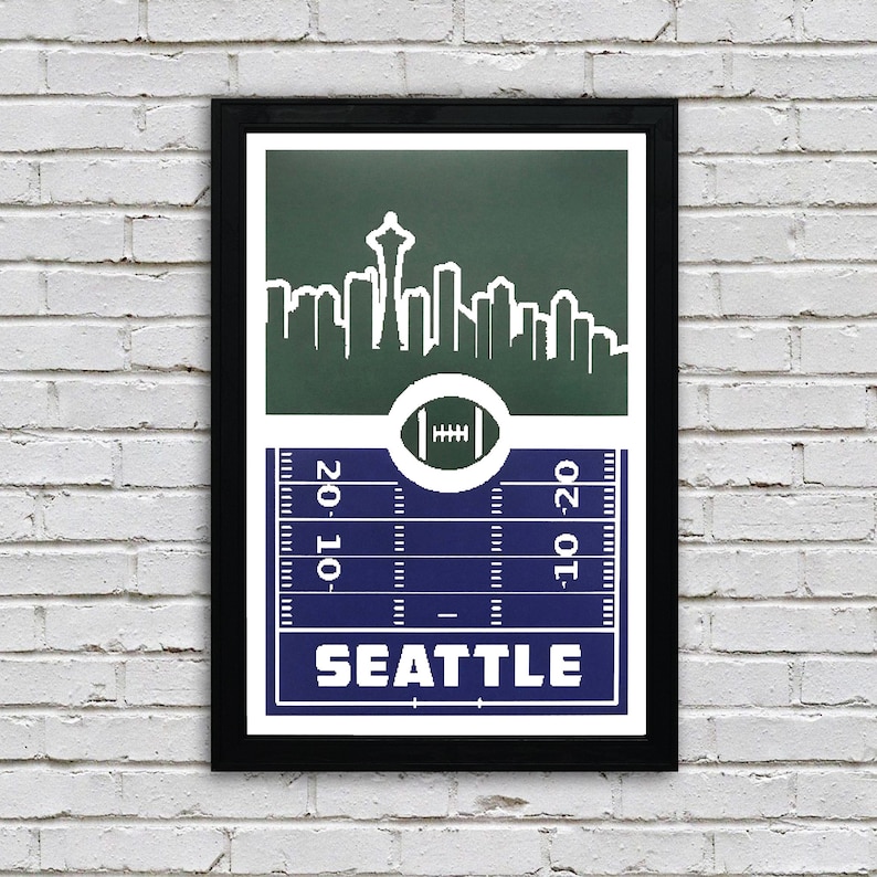 May include: A green and blue football field print with a white silhouette of the Seattle skyline, including the Space Needle, and the word "SEATTLE" in white text.