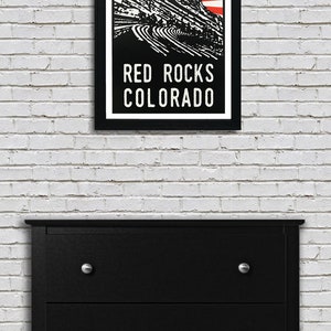K&ouml;nnte beinhalten: Eine Schwarzwei&szlig;illustration des Red Rocks Amphitheaters in Morrison, Colorado. Die Illustration ist vor einem roten und wei&szlig;en Sonnenstrahlenhintergrund platziert. Der Text "RED ROCKS COLORADO" ist unter der Illustration gedruckt.