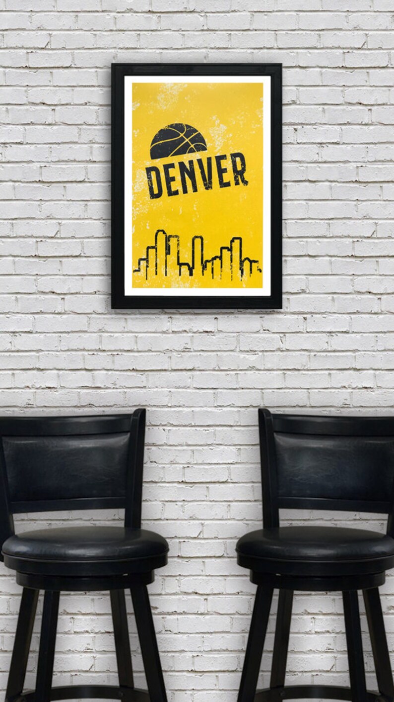 Puede incluir: Un p&oacute;ster enmarcado en negro con fondo amarillo y un gr&aacute;fico de baloncesto. El texto "DENVER" est&aacute; en letras negras en el p&oacute;ster. El p&oacute;ster est&aacute; colgado en una pared de ladrillo blanco. Dos taburetes de bar negros est&aacute;n frente a la pared.