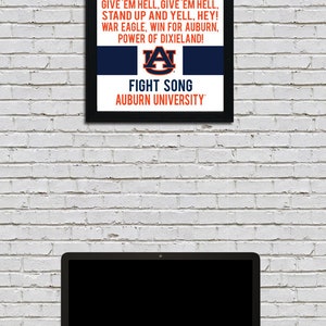 K&ouml;nnte beinhalten: Ein gerahmter Druck mit einem schwarzen Rahmen und einem wei&szlig;en Hintergrund. Der Druck zeigt die Textzeilen des Kampfliedes der Auburn University und das Logo der Auburn University in Orange und Blau. Der Text lautet "War Eagle, Fly Down the Field, Ever to Conquer, Never to Yield: War Eagle. Fearless and True. Fight on You Orange and Blue. Go! Go! Go! On to Victory, Strike Up the Band. Give 'Em Hell, Give 'Em Hell, Stand Up and Yell, Hey! War Eagle, Win for Auburn, Power of Dixieland!" Das Logo ist ein stilisiertes "A" mit einem Tigerkopf darin. Der Text "Fight Song" und "Auburn University" befindet sich unter dem Logo.