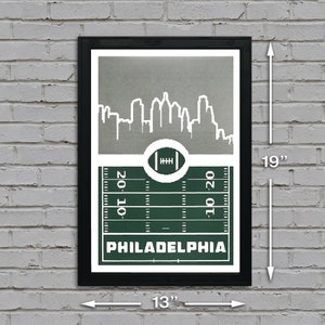 May include: A black framed print with a green and white football field design. The print features a white silhouette of the Philadelphia skyline and the text "PHILADELPHIA". The print measures 13 inches wide by 19 inches tall.