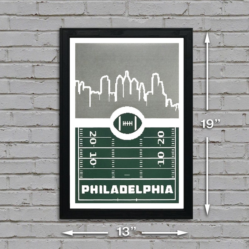 May include: A black framed print with a green and white football field design. The print features a white silhouette of the Philadelphia skyline and the text "PHILADELPHIA". The print measures 13 inches wide by 19 inches tall.