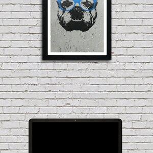 May include: A black and white illustration of a bulldog wearing blue glasses. The illustration is framed in a black frame and is hanging on a white brick wall.