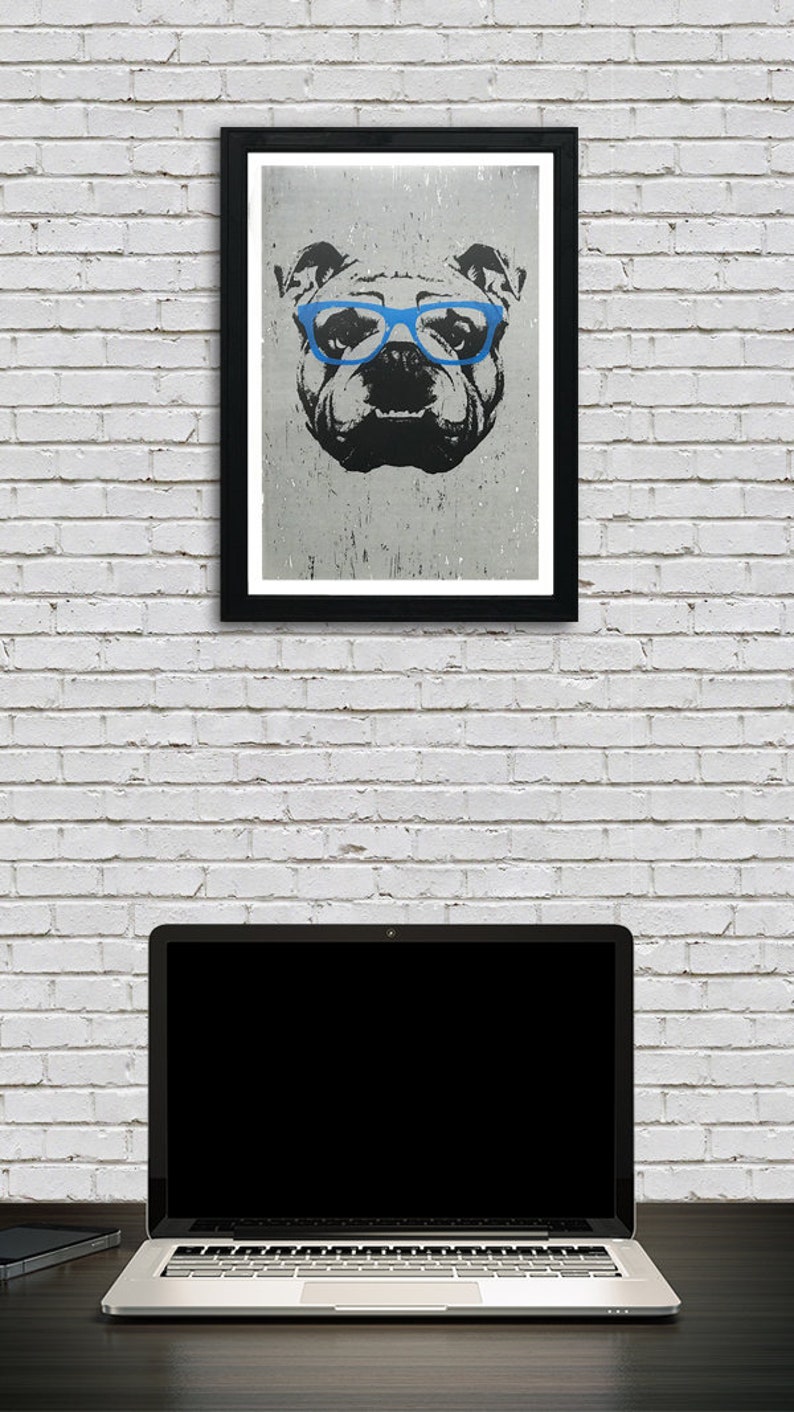 May include: A black and white illustration of a bulldog wearing blue glasses. The illustration is framed in a black frame and is hanging on a white brick wall.