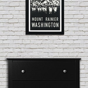 May include: A black framed poster with a green and white illustration of Mount Rainier in Washington state. The text "MOUNT RAINIER WASHINGTON" is printed in white below the illustration.