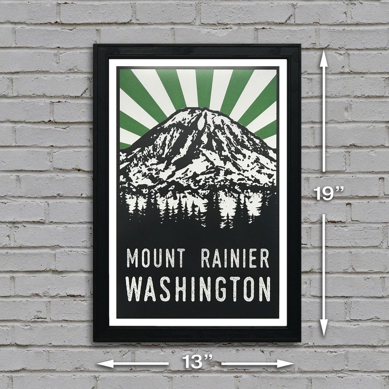 May include: A black framed poster with a green and white sunburst design behind a black and white illustration of Mount Rainier. The text "Mount Rainier Washington" is printed in white at the bottom of the poster. The poster measures 13 inches wide by 19 inches tall.