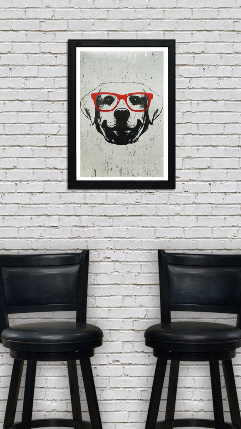 May include: A black and white illustration of a dog wearing red glasses. The illustration is framed in a black frame and hanging on a white brick wall. Two black bar stools are in the foreground.