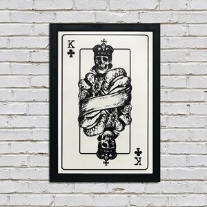 May include: A black and white illustration of the King of Clubs playing card. The King is depicted as a skull wearing a crown and surrounded by flowers and a banner.