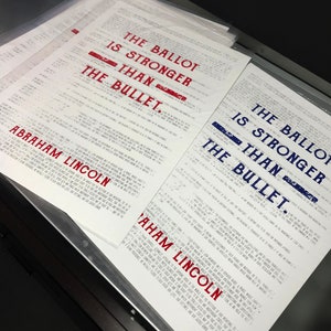 May include: A close-up of a stack of white papers with the text "The Ballot is Stronger Than The Bullet." printed in red and blue. The text is attributed to Abraham Lincoln.
