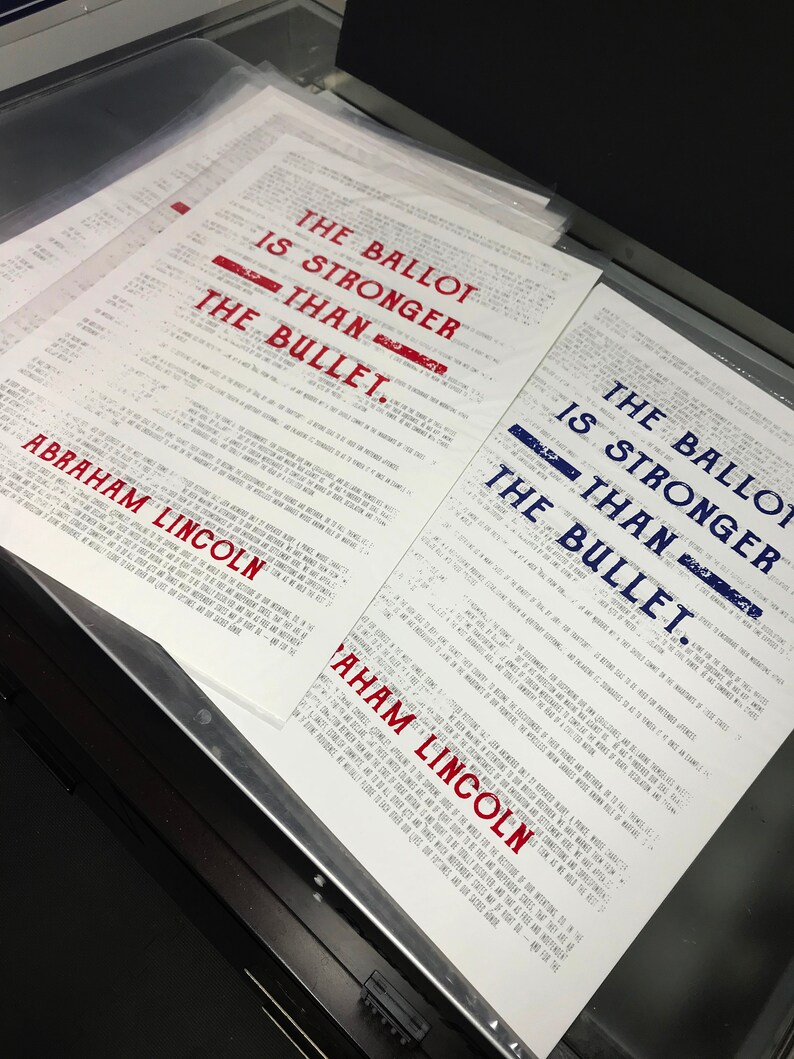 May include: A close-up of a stack of white papers with the text "The Ballot is Stronger Than The Bullet." printed in red and blue. The text is attributed to Abraham Lincoln.