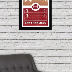 May include: A framed print of a red and white football field with a white silhouette of the San Francisco skyline. The text "SAN FRANCISCO" is printed below the field.