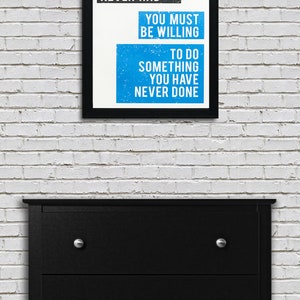 May include: A black framed motivational poster with white text on a blue background. The text reads "If you want something you have never had you must be willing to do something you have never done."