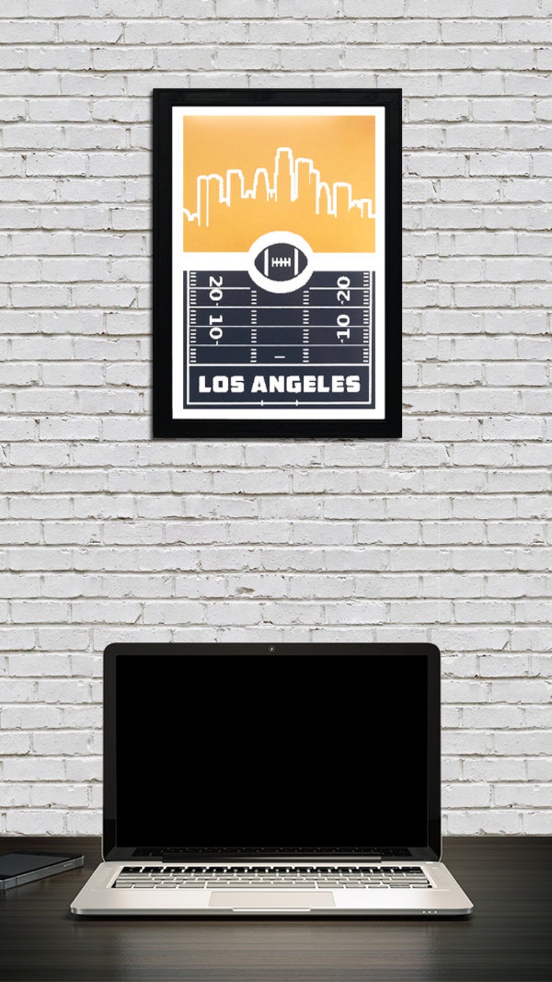 May include: A framed print with a gold skyline of Los Angeles and a football field graphic with the text "20-10" and "10-20" on the yard lines. The text "LOS ANGELES" is at the bottom of the print.