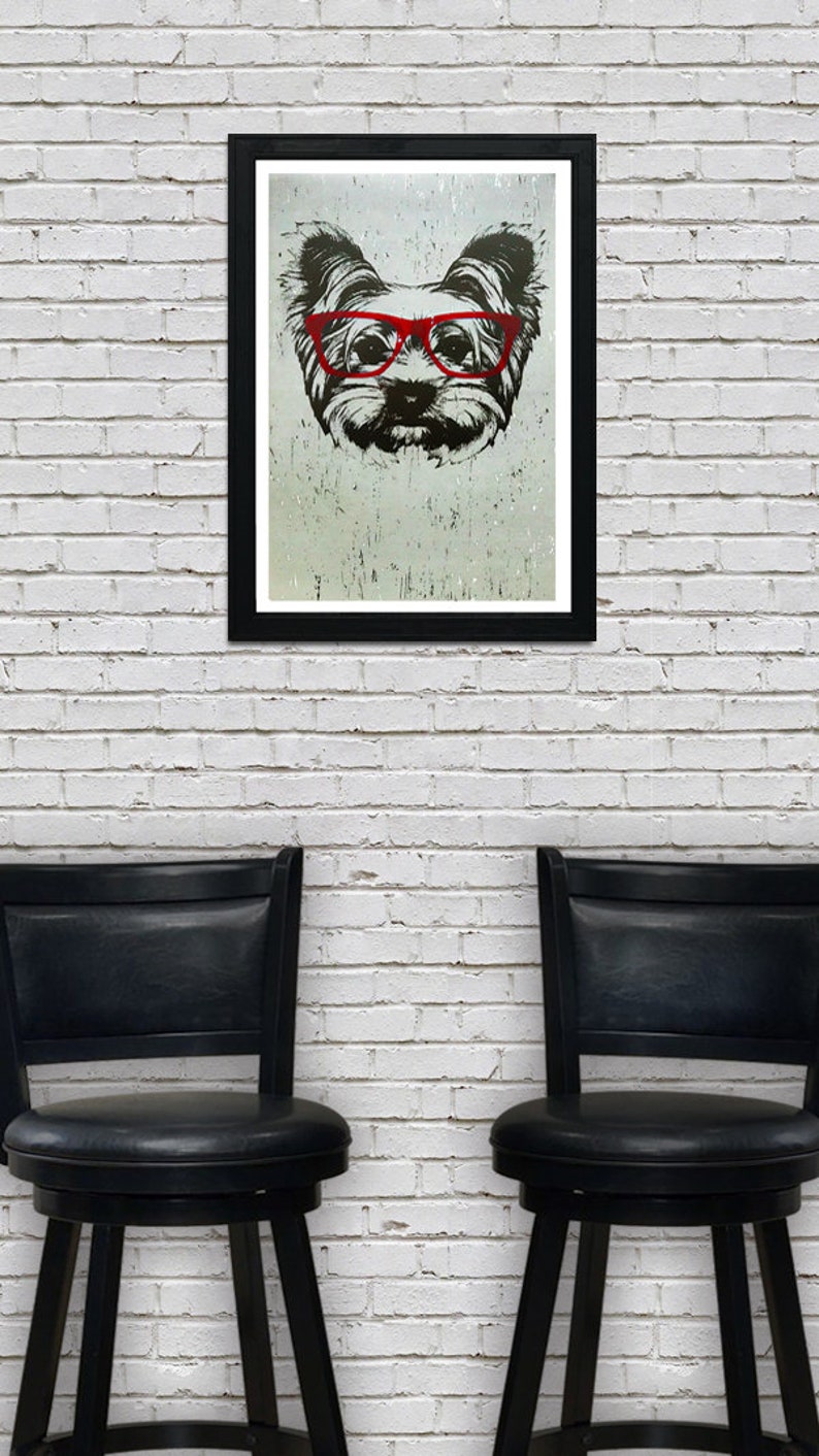 May include: A black and white illustration of a dog wearing red glasses. The dog is in a framed print, hanging on a white brick wall. Two black bar stools are in the foreground.