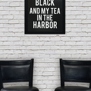 May include: Black and white framed sign with the text "I like my coffee black and my tea in the harbor". Two black bar stools are in front of the sign against a white brick wall.