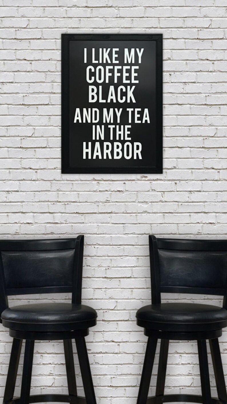 May include: Black and white framed sign with the text "I like my coffee black and my tea in the harbor". Two black bar stools are in front of the sign against a white brick wall.