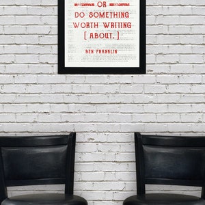 May include: A framed black and white print with a quote by Ben Franklin that reads "Either write something worth reading or do something worth writing about." The quote is in red text. The print is hanging on a white brick wall. Two black bar stools are in front of the wall.