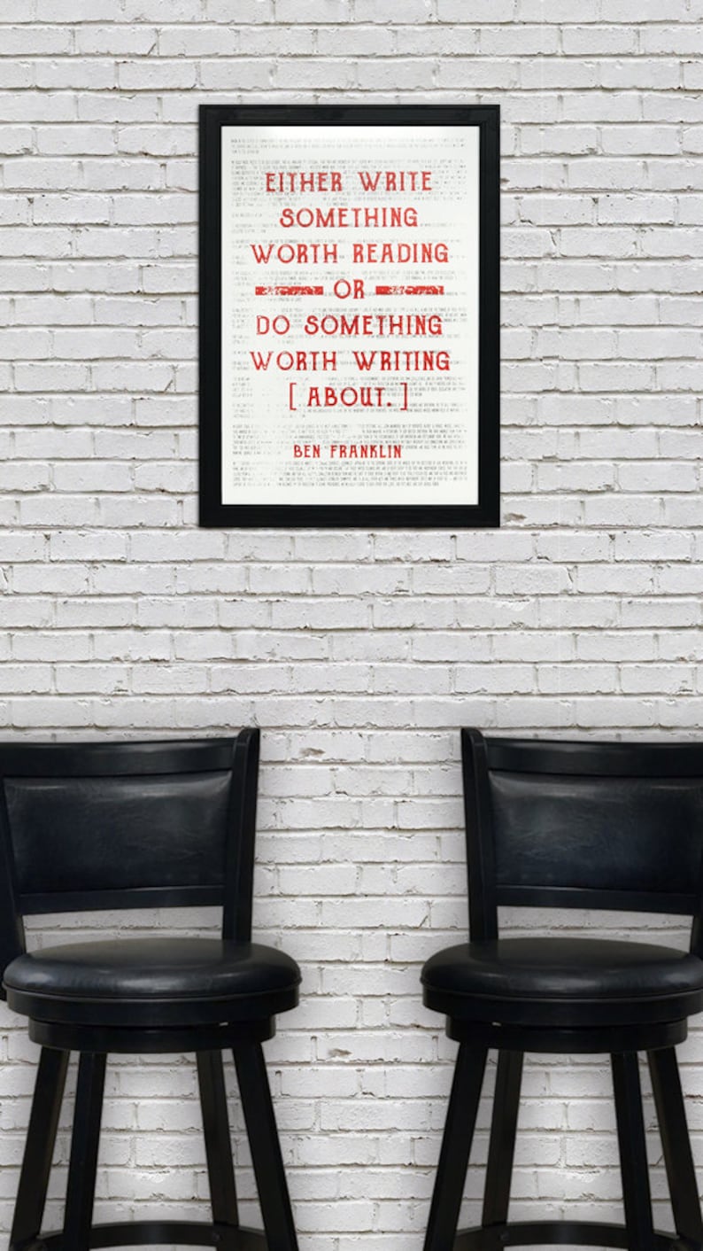 May include: A framed black and white print with a quote by Ben Franklin that reads "Either write something worth reading or do something worth writing about." The quote is in red text. The print is hanging on a white brick wall. Two black bar stools are in front of the wall.