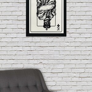 May include: A black and white illustration of the King of Clubs playing card. The King is depicted as a skeleton wearing a crown and wrapped in a banner. The card is framed in black.