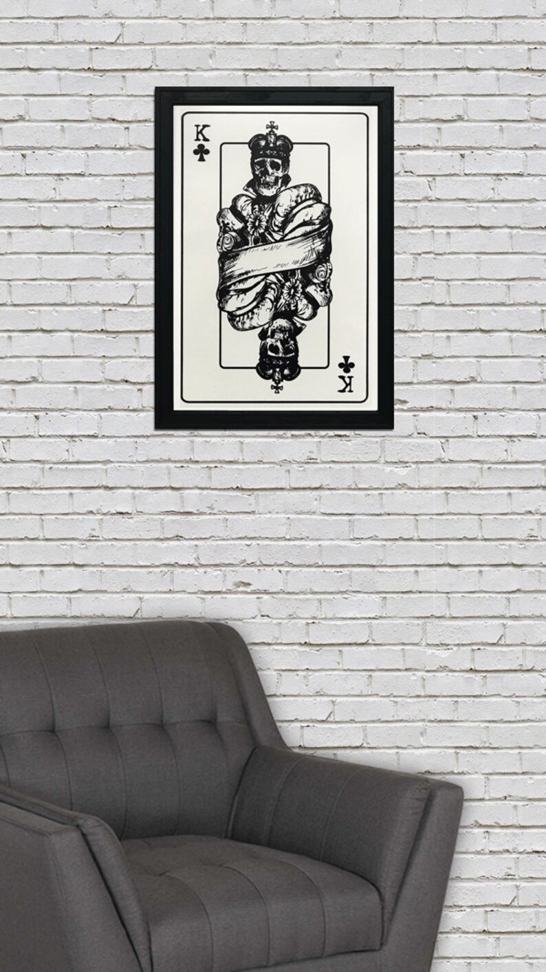 May include: A black and white illustration of the King of Clubs playing card. The King is depicted as a skeleton wearing a crown and wrapped in a banner. The card is framed in black.