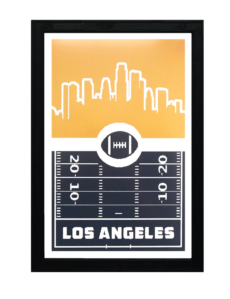 May include: A framed print with a gold background featuring a white silhouette of the Los Angeles skyline. The bottom of the print shows a black and white football field with a football in the center and the text "LOS ANGELES" below.