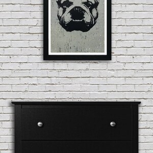 Puede incluir: Una ilustraci&oacute;n en blanco y negro de la cara de un bulldog en un marco negro contra una pared de ladrillo blanco. La cara del bulldog est&aacute; centrada en el marco y tiene una expresi&oacute;n seria. La imagen est&aacute; impresa en un papel texturizado.