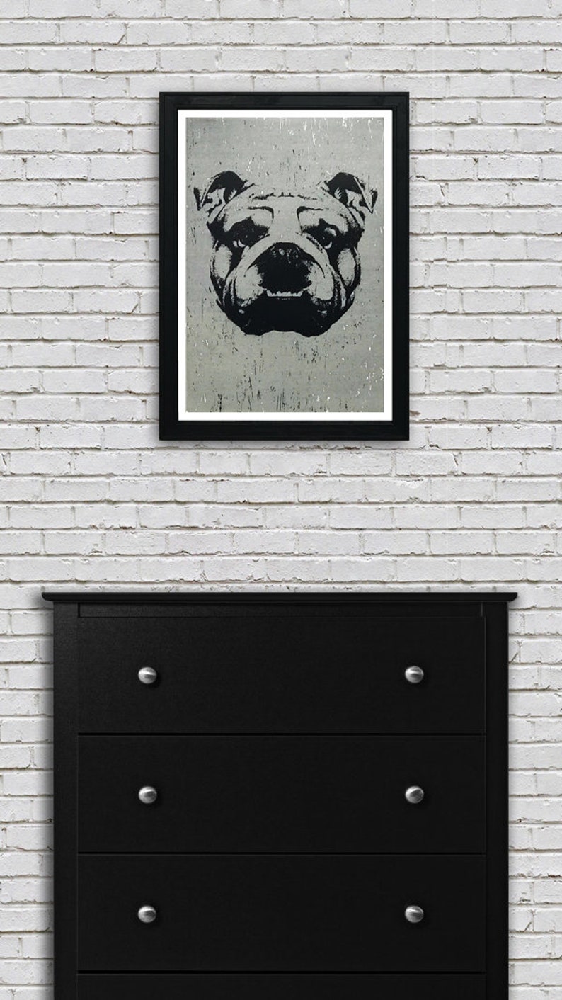 Puede incluir: Una ilustraci&oacute;n en blanco y negro de la cara de un bulldog en un marco negro contra una pared de ladrillo blanco. La cara del bulldog est&aacute; centrada en el marco y tiene una expresi&oacute;n seria. La imagen est&aacute; impresa en un papel texturizado.