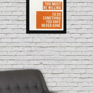 May include: A motivational quote in a black frame on a white brick wall. The quote reads: "If you want something you have never had, you must be willing to do something you have never done."
