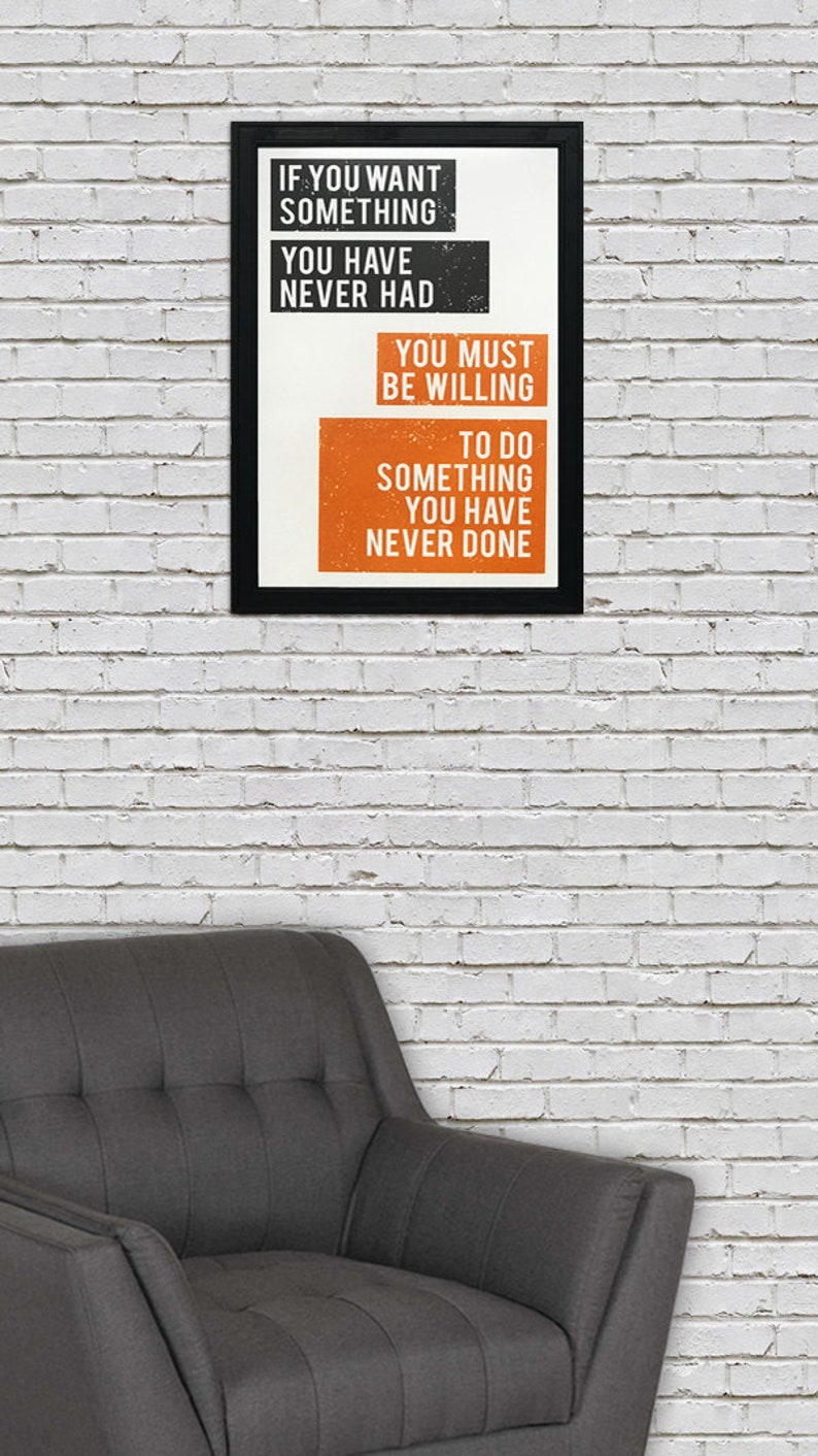 May include: A motivational quote in a black frame on a white brick wall. The quote reads: "If you want something you have never had, you must be willing to do something you have never done."