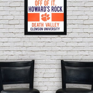 May include: A black framed poster with an orange and white background. The poster reads "Give me 110% or keep your filthy hands off of it. Howard's Rock. Death Valley. Clemson University."