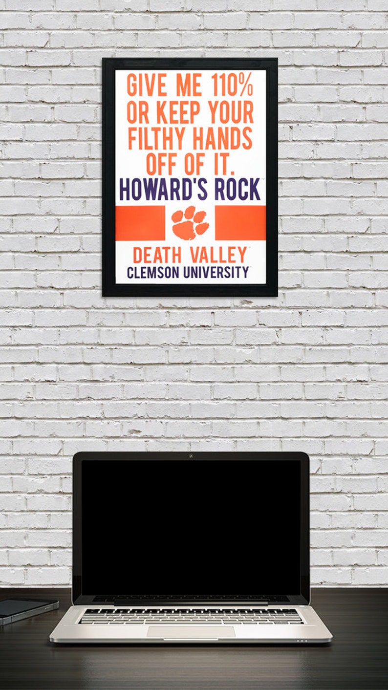 May include: A black framed poster with orange and purple text that reads "Give me 110% or keep your filthy hands off of it. Howard's Rock. Death Valley. Clemson University". The poster has a paw print graphic in the center.
