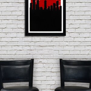 May include: A framed art print featuring the Denver skyline in black against a red background, with the city name in white. The text reads "DENVER THE MILE HIGH CITY." Below, two black bar stools are positioned in front of a white brick wall.