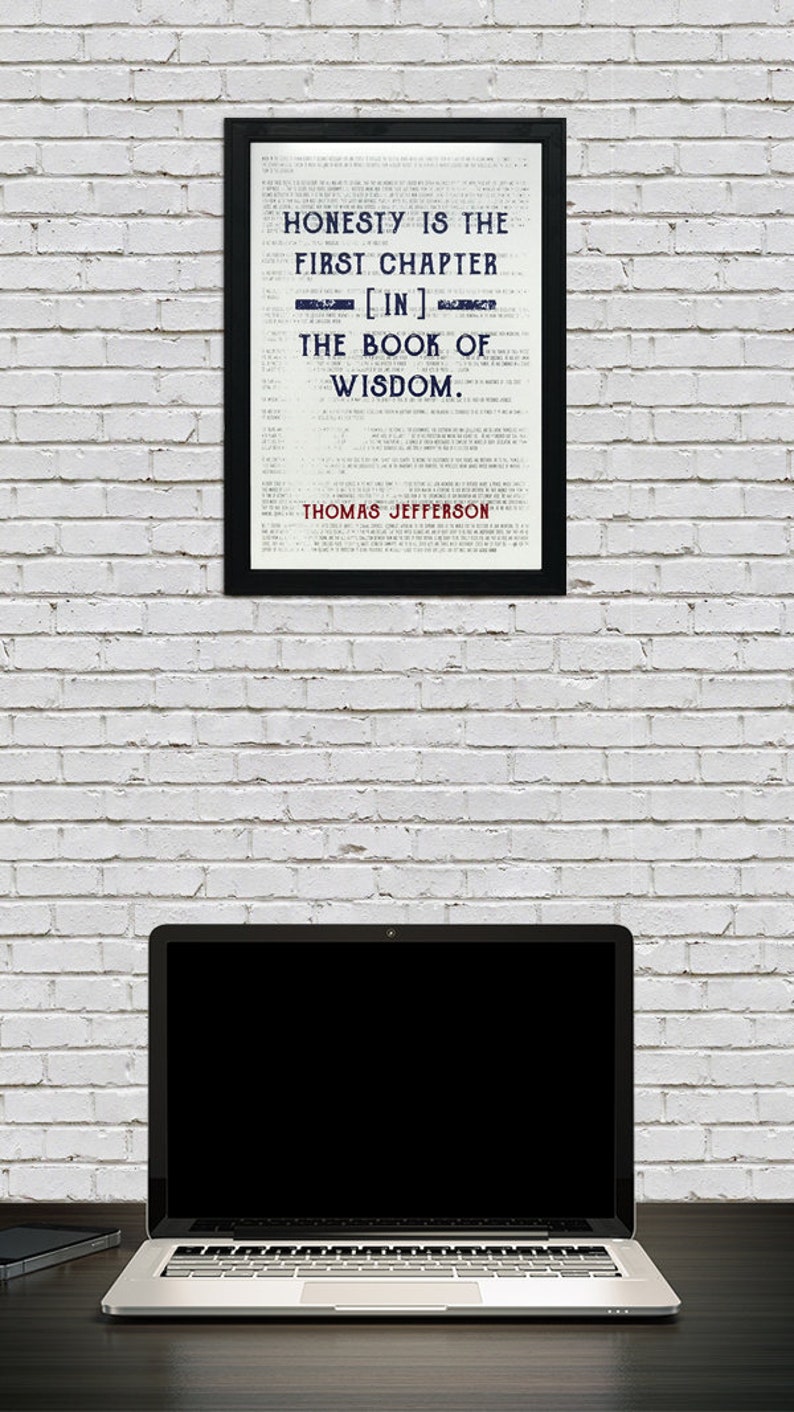 May include: A framed print with the quote "Honesty is the first chapter [in] the book of wisdom" by Thomas Jefferson. A laptop computer sits on a desk below the framed print, against a white brick wall.