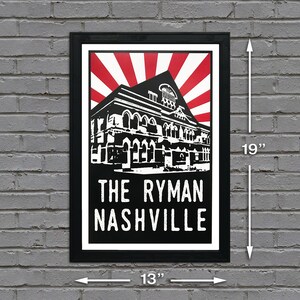May include: Black and white poster with a red and white sunburst design. The poster features a stylised illustration of the Ryman Auditorium in Nashville, Tennessee. The text "The Ryman Nashville" is printed in white at the bottom of the poster. The poster is framed in a black frame and measures 13 inches wide by 19 inches tall.