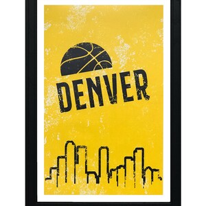 Puede incluir: Un p&oacute;ster amarillo con una pelota de baloncesto negra y la palabra "DENVER" en texto negro. El p&oacute;ster tambi&eacute;n presenta una silueta negra del horizonte de Denver.