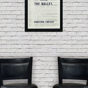 May include: A black framed print with a white background and the text "The ballot is stronger than the bullet. Abraham Lincoln." The print is hanging on a white brick wall. Two black bar stools are in front of the print.