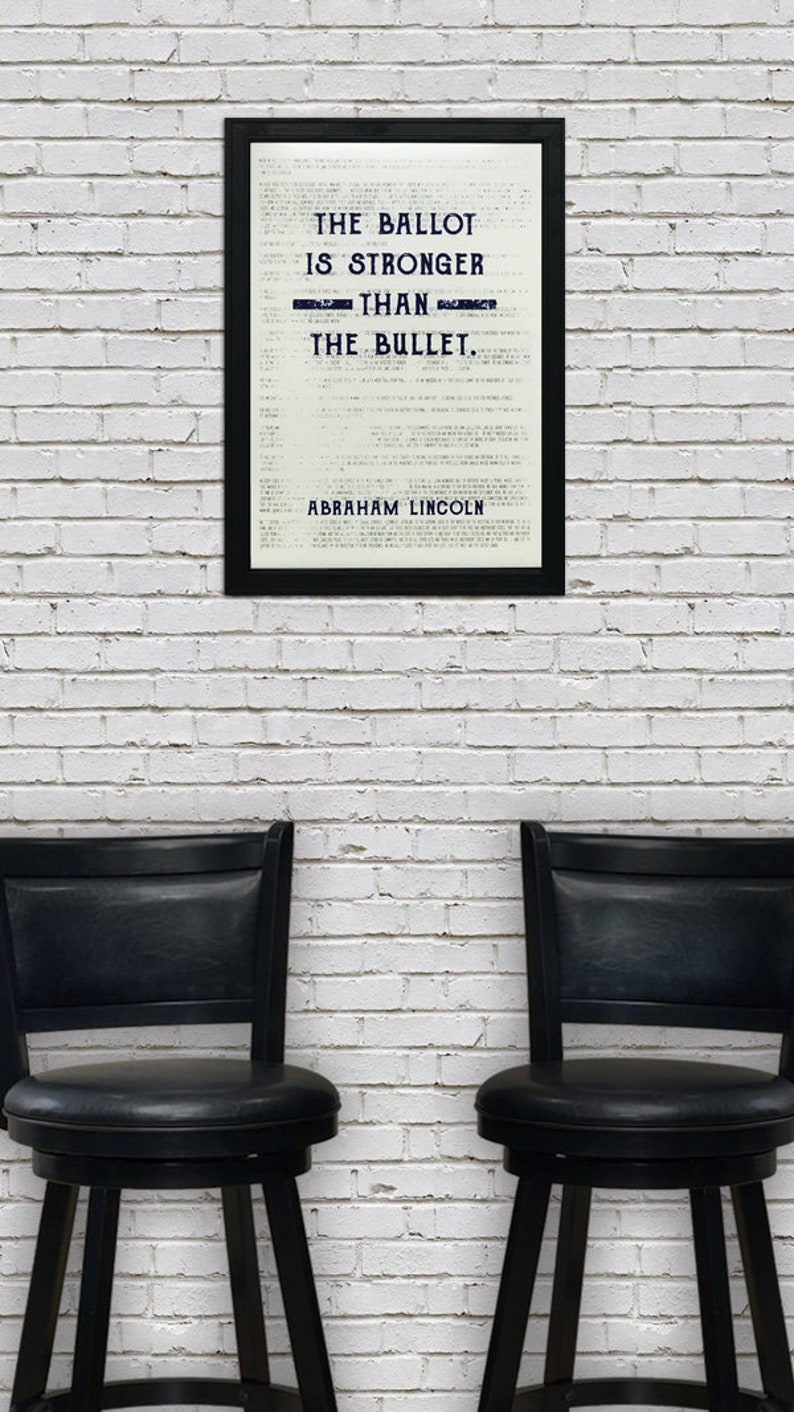 May include: A black framed print with a white background and the text "The ballot is stronger than the bullet. Abraham Lincoln." The print is hanging on a white brick wall. Two black bar stools are in front of the print.